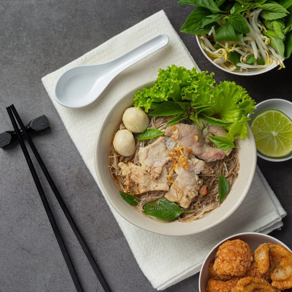 Vietnamese pho with pork, meatballs, and fresh herbs, served with crispy pork rinds and lime.
